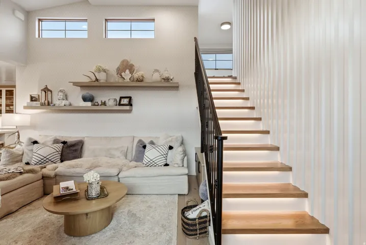 Light-filled living space featuring floor-to-ceiling windows, floating wood shelving, a round wood-finish coffee table, and a geometric patterned sofa