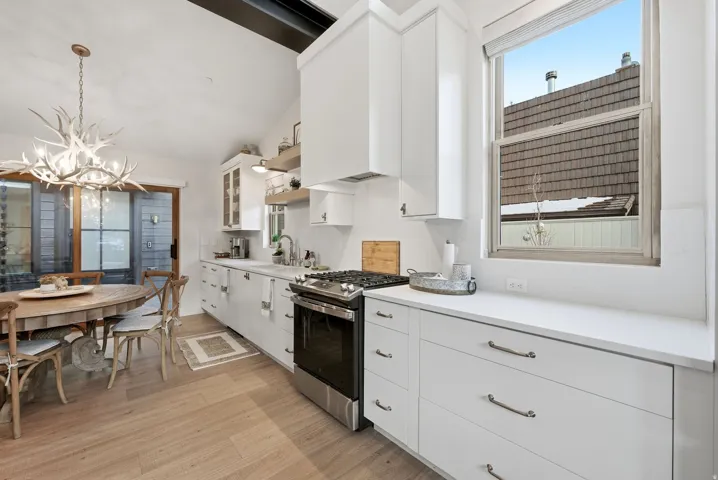 Vaulted ceiling, wood-finish flooring, white cabinetry with contemporary hardware, stainless steel range, and a large window