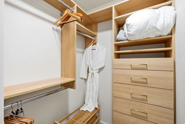 Custom closet system featuring wood-finish shelving, multiple hanging rods, built-in drawers with gold-tone pulls, and integrated open storage