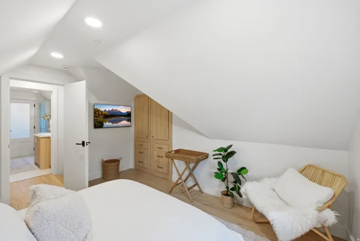 Sloped ceiling with recessed lighting, wood-finish flooring, built-in wood cabinetry, and a wall-mounted television
