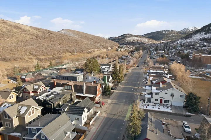 Aerial perspective of a residential street with diverse architectural styles, framed by rolling hillsides and distant snow-capped mountains