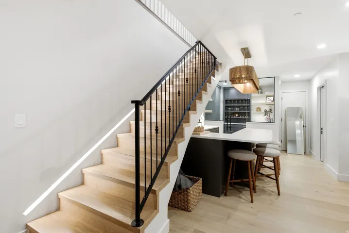 Hardwood staircase with wrought iron railing, open-concept kitchen with island seating, pendant lighting, and light wood-finish flooring