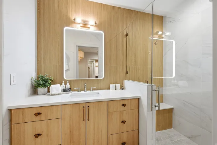 Wood-finish vanity with a light-toned countertop, integrated sink, and an illuminated mirror