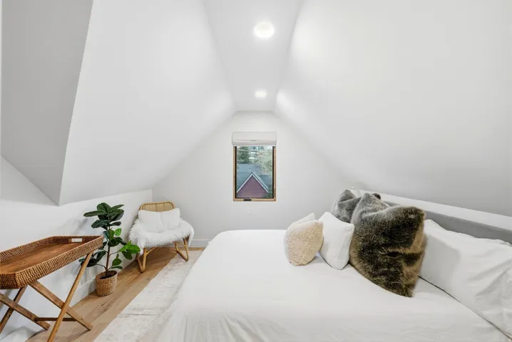 Vaulted ceiling with recessed lighting, light wood-finish flooring, and a window with blinds