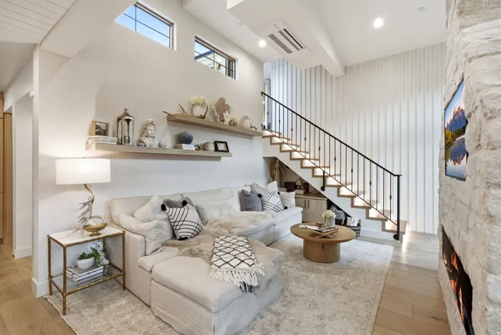 Stone-clad fireplace with built-in media, wood-finish flooring, floating wood shelving, and integrated staircase lighting