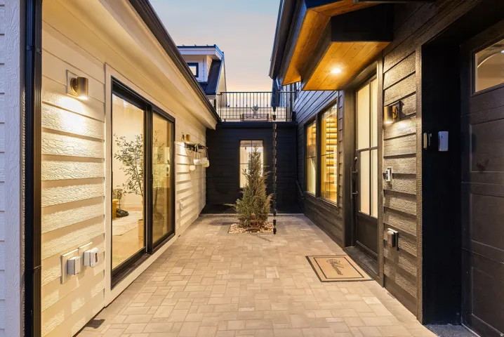 Modern courtyard entry featuring warm wood-finish siding, glass-panel doors with horizontal detailing, herringbone-pattern paver flooring, and integrated landscape lighting