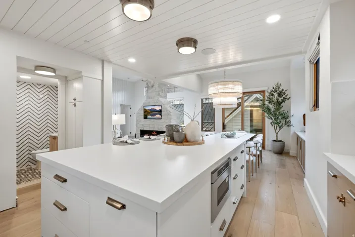 Kitchen island with integrated microwave, wood-finish flooring, white shiplap ceiling, and stone fireplace with built-in television