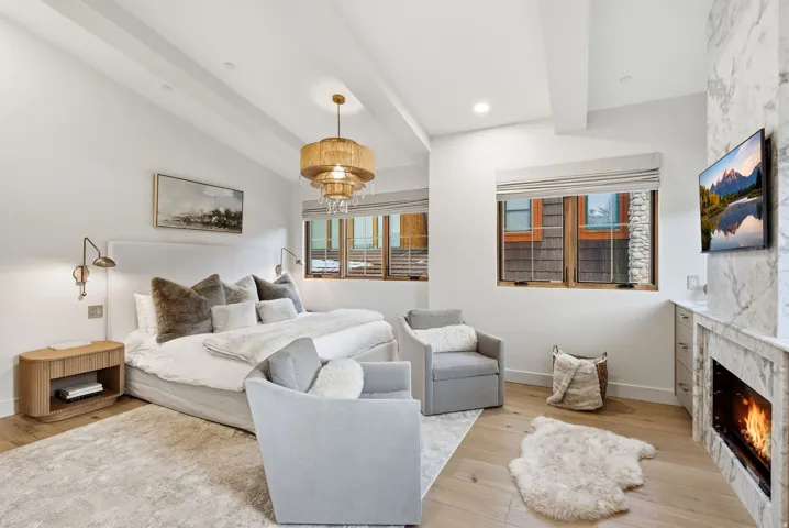 Hardwood-style flooring, tray ceiling, integrated fireplace with stone surround, wall-mounted light fixtures, and a modern chandelier
