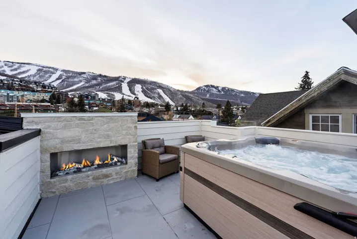 Rooftop patio with a built-in fireplace, hot tub, and stone accent wall