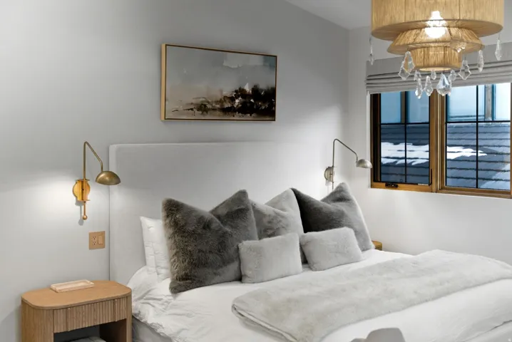 Upholstered headboard, wood-frame window, dual wall-mounted sconces, and a tiered chandelier with crystal accents