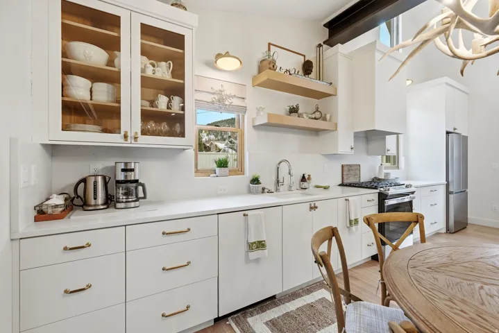 Kitchen featuring white cabinetry, brass hardware, wood-finish flooring, stainless steel appliances, and a vaulted ceiling with exposed beam