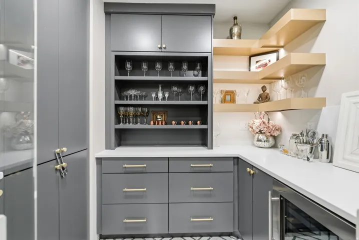 Built-in cabinetry with gold-tone hardware, a beverage cooler, floating wood shelving, and a white countertop