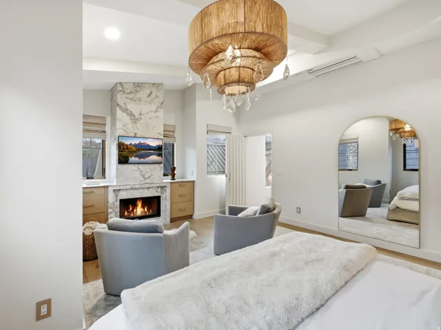 Stone-clad fireplace with built-in cabinetry, wood-finish flooring, an arched mirror, and a tiered chandelier