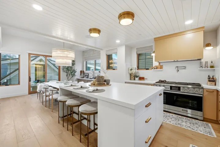 Spacious kitchen featuring a large central island with seating, stainless steel range with pot filler, wood-finish flooring, white paneled ceiling, and sliding glass doors