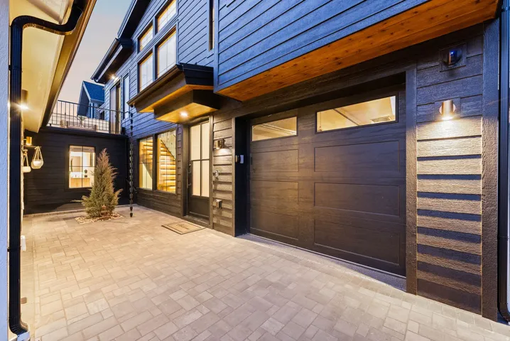Modern exterior featuring dark horizontal siding, an integrated garage with transom windows, a paver driveway, and contemporary outdoor lighting