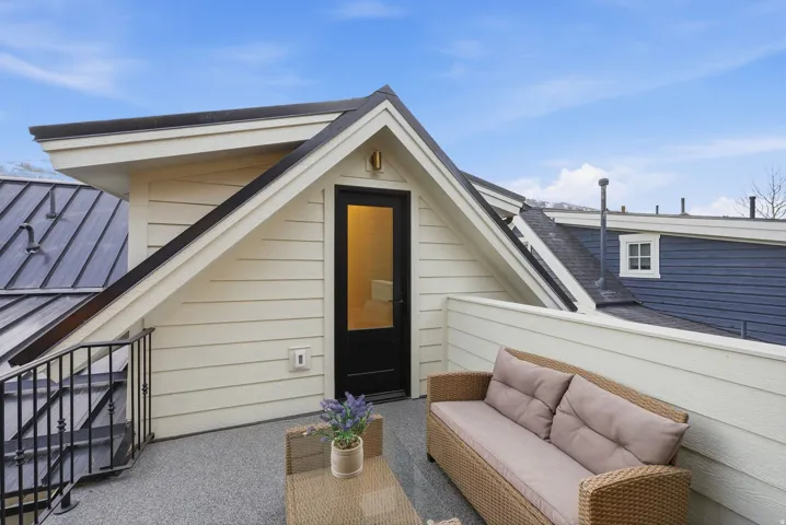Rooftop deck featuring composite decking, woven rattan seating with cushioned comfort, and a contemporary black entry door with glass panel