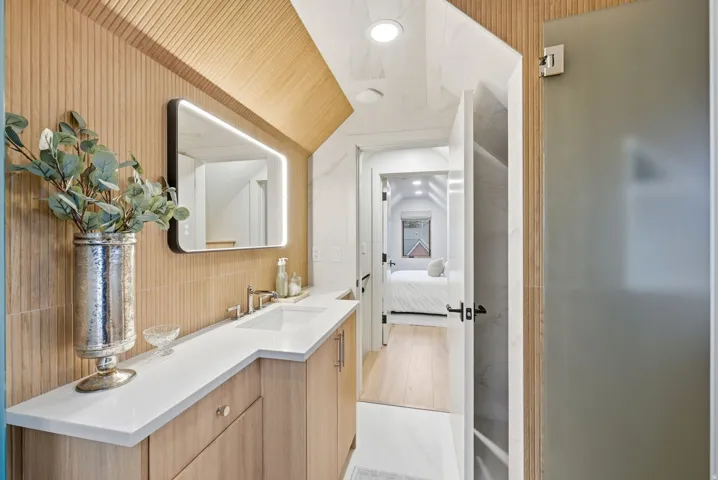 Wood-finish wall paneling, white countertop, integrated sink, and illuminated mirror