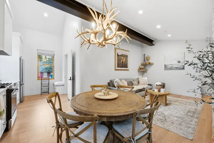 Vaulted ceilings with exposed beam, recessed lighting, wood-finish flooring, and white cabinetry with stainless steel appliances