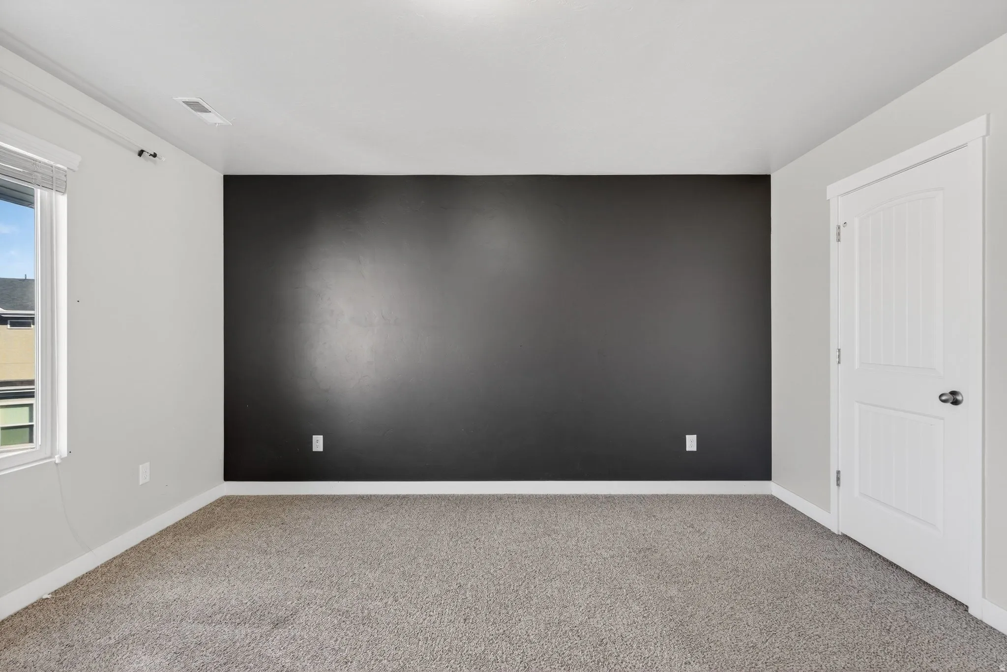 Carpeted room featuring a dark accent wall, white trim, and a paneled door with black hardware