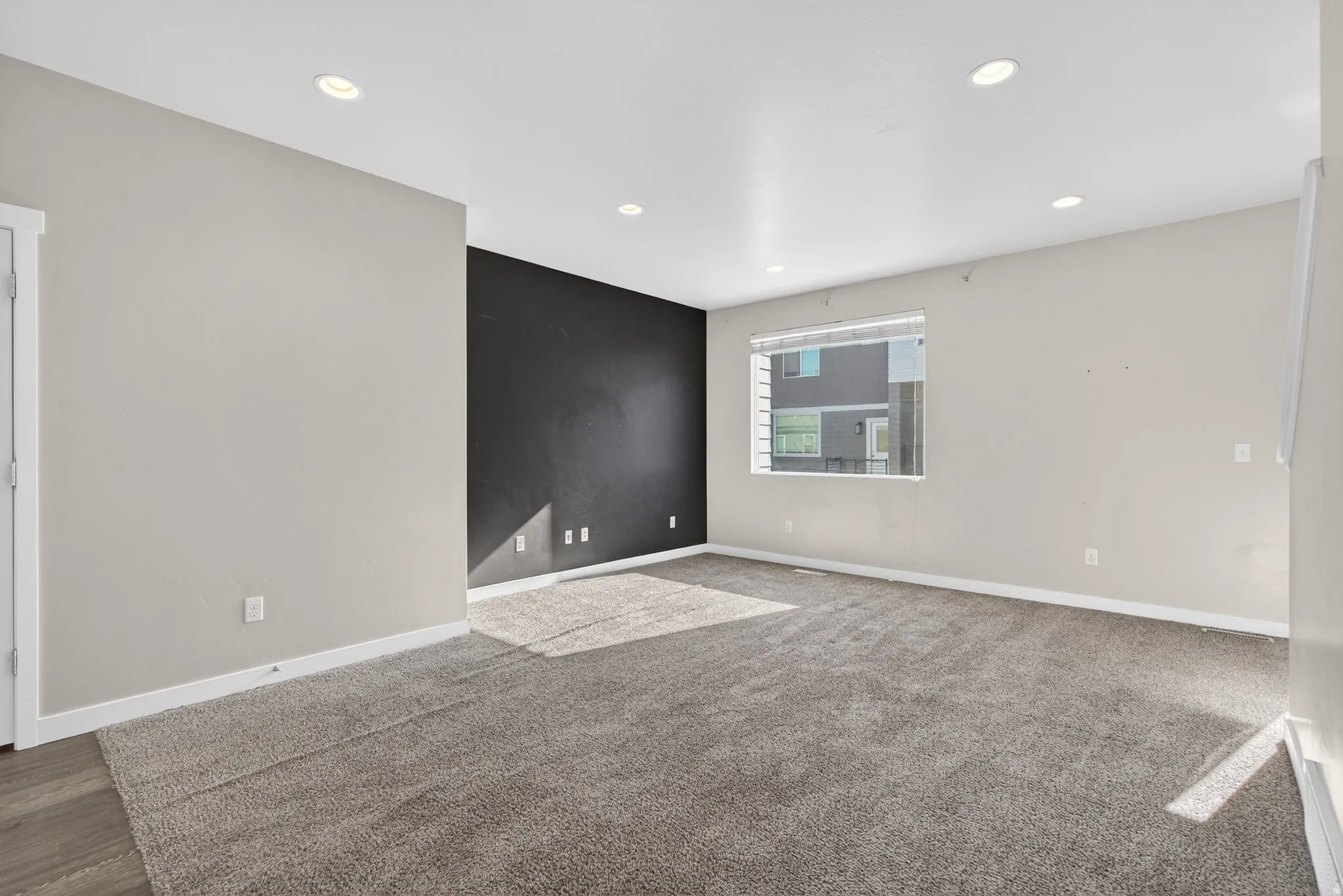 Expansive carpeted area with recessed lighting, a contrasting accent wall, and a window with blinds