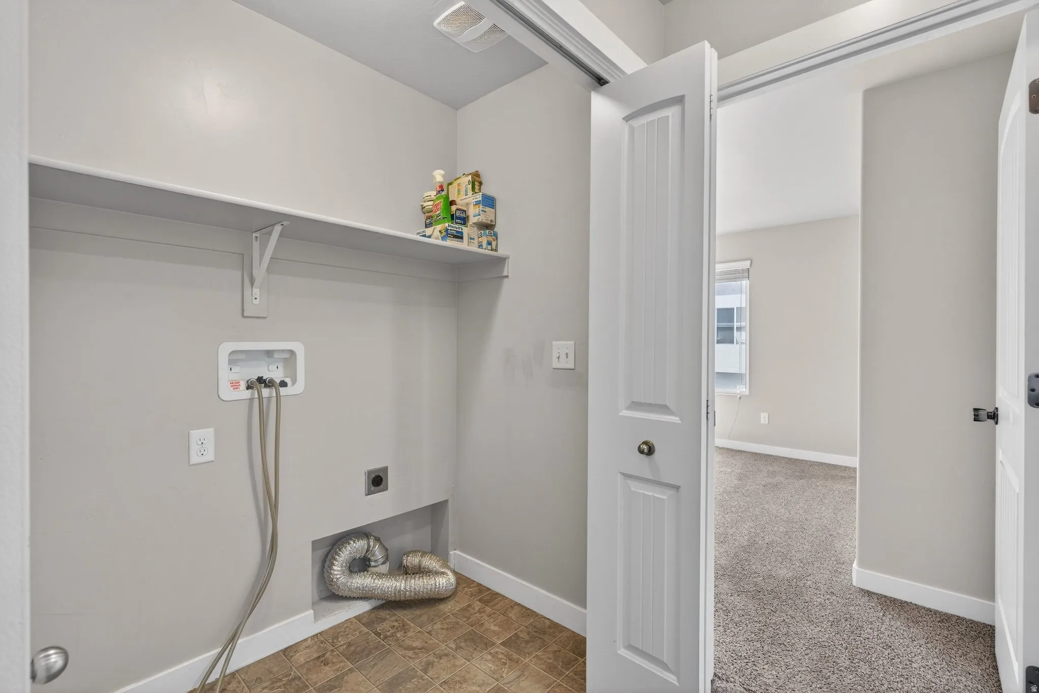 Dedicated laundry room featuring a front-load washer hookup with integrated shelving, cork-finish flooring, and direct access to the primary closet space