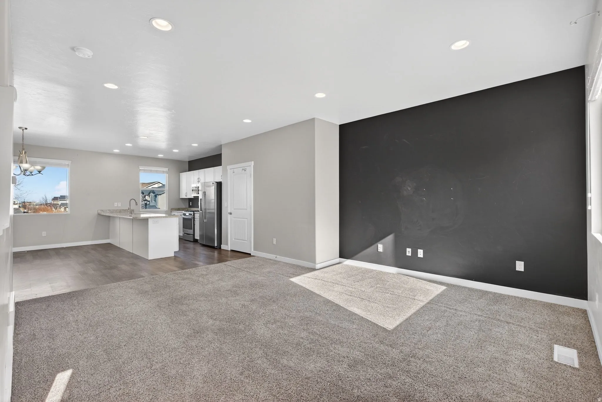 Open-concept living area with neutral carpeting and a dark accent wall
