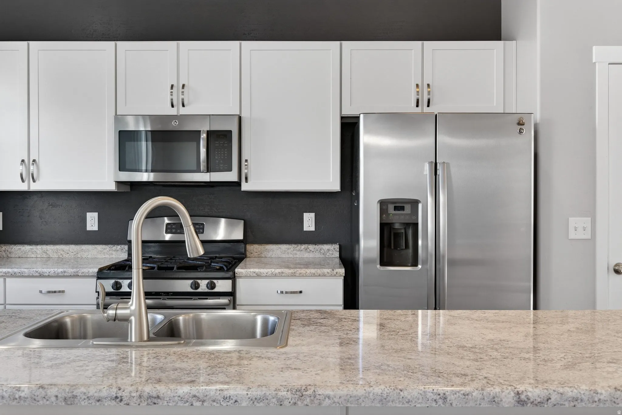 White cabinetry, stainless steel appliances, dual basin sink, pull-down faucet, and light-toned countertops