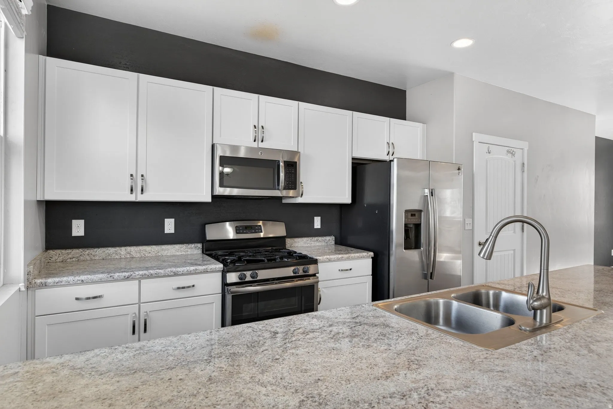Kitchen featuring a dual basin stainless steel sink, stainless steel appliances, white cabinetry, and light-toned countertops