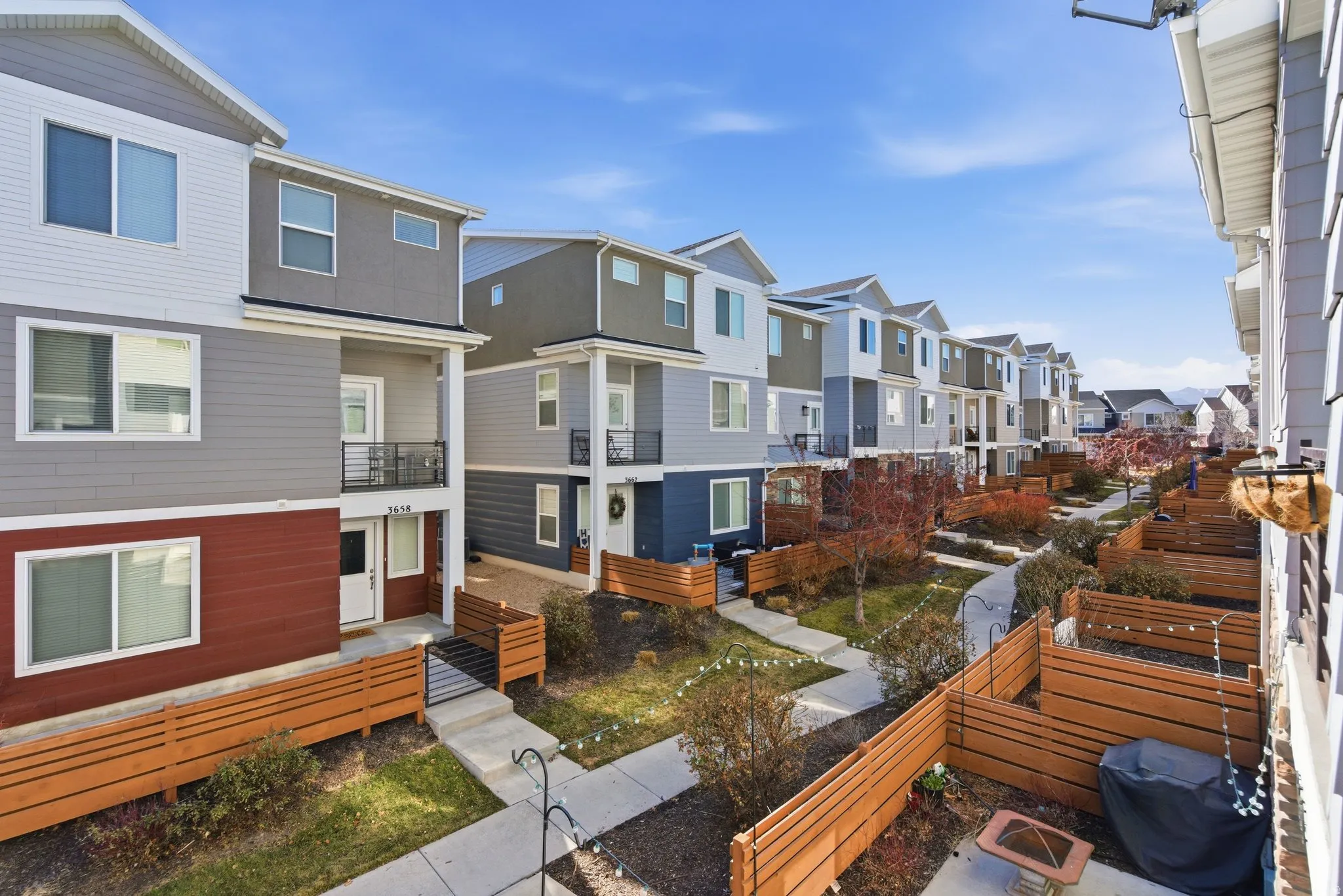 Modern townhome exterior featuring multi-toned siding, private balconies with metal railings, and individual fenced patios
