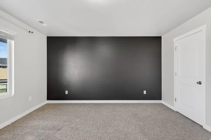 Carpeted room featuring a dark accent wall, white trim, and a paneled door with black hardware
