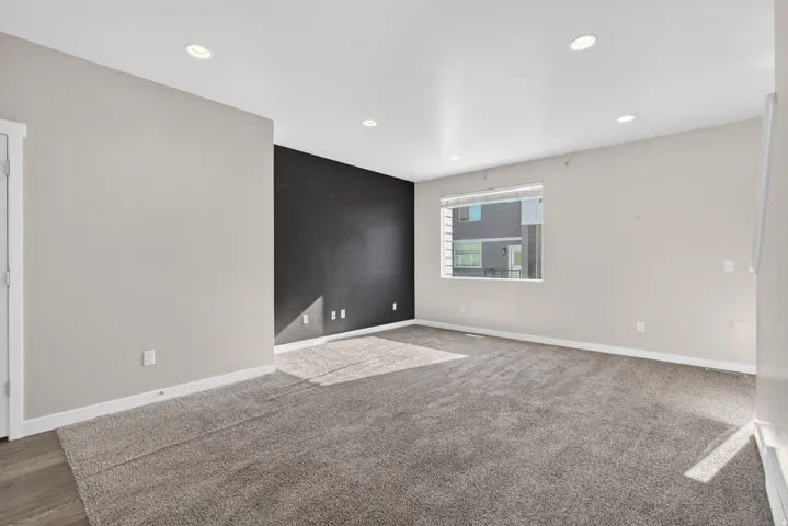 Expansive carpeted area with recessed lighting, a contrasting accent wall, and a window with blinds