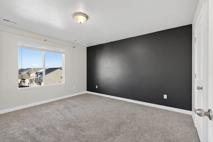 Neutral wall color with an accent wall, window with blinds, carpeted flooring, and a flush-mount ceiling light fixture