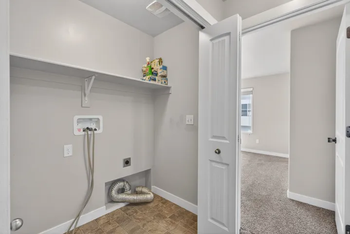 Dedicated laundry room featuring a front-load washer hookup with integrated shelving, cork-finish flooring, and direct access to the primary closet space