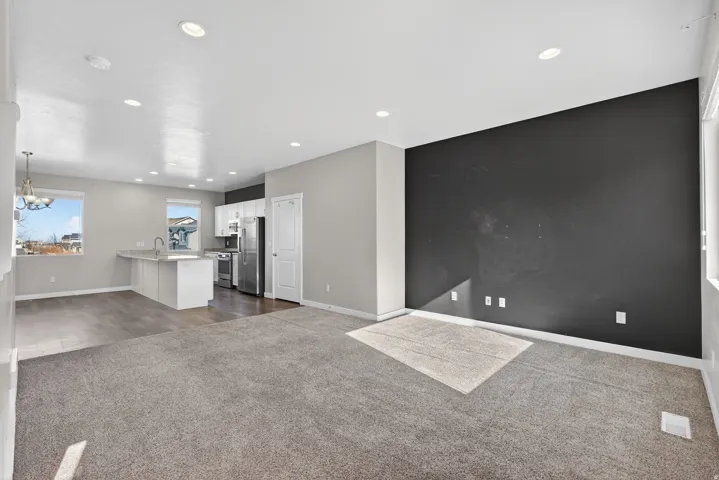 Open-concept living area with neutral carpeting and a dark accent wall
