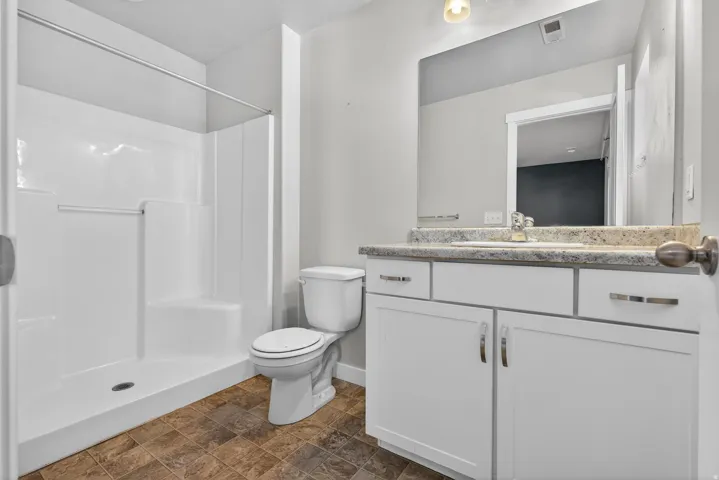 Bathroom featuring a shower stall, toilet, vanity with integrated sink, and a framed mirror