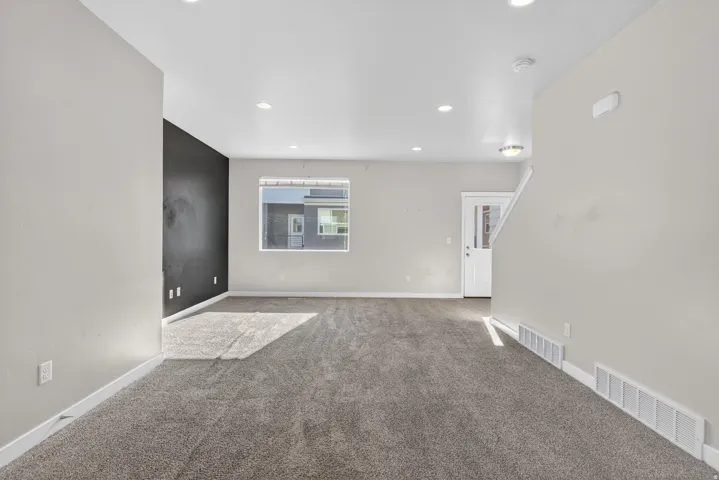Expansive room featuring plush carpeting, recessed lighting, a contrasting accent wall, and a window with exterior visibility