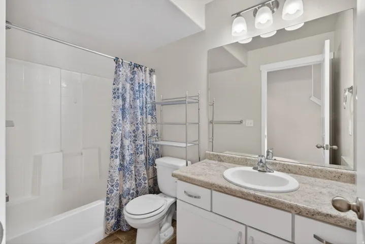 Bathroom featuring a full-size tub with shower, white vanity with an integrated sink, stone-finish countertop, and wall-mounted light fixture