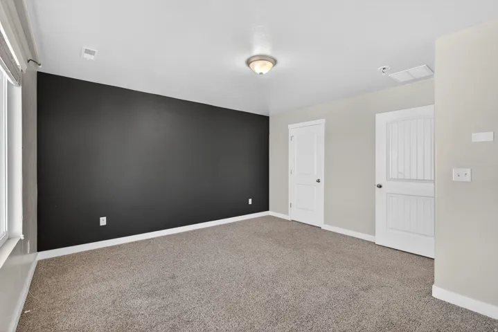 Carpeted room featuring a dark accent wall, two panel doors, a window with blinds, and a ceiling-mounted light fixture