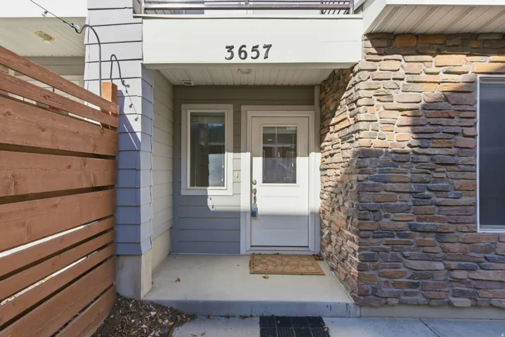 Stone veneer facade with siding accents, a prominent house number, and a wood-slat privacy fence