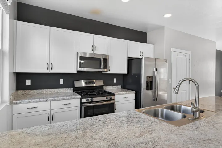 Kitchen featuring a dual basin stainless steel sink, stainless steel appliances, white cabinetry, and light-toned countertops
