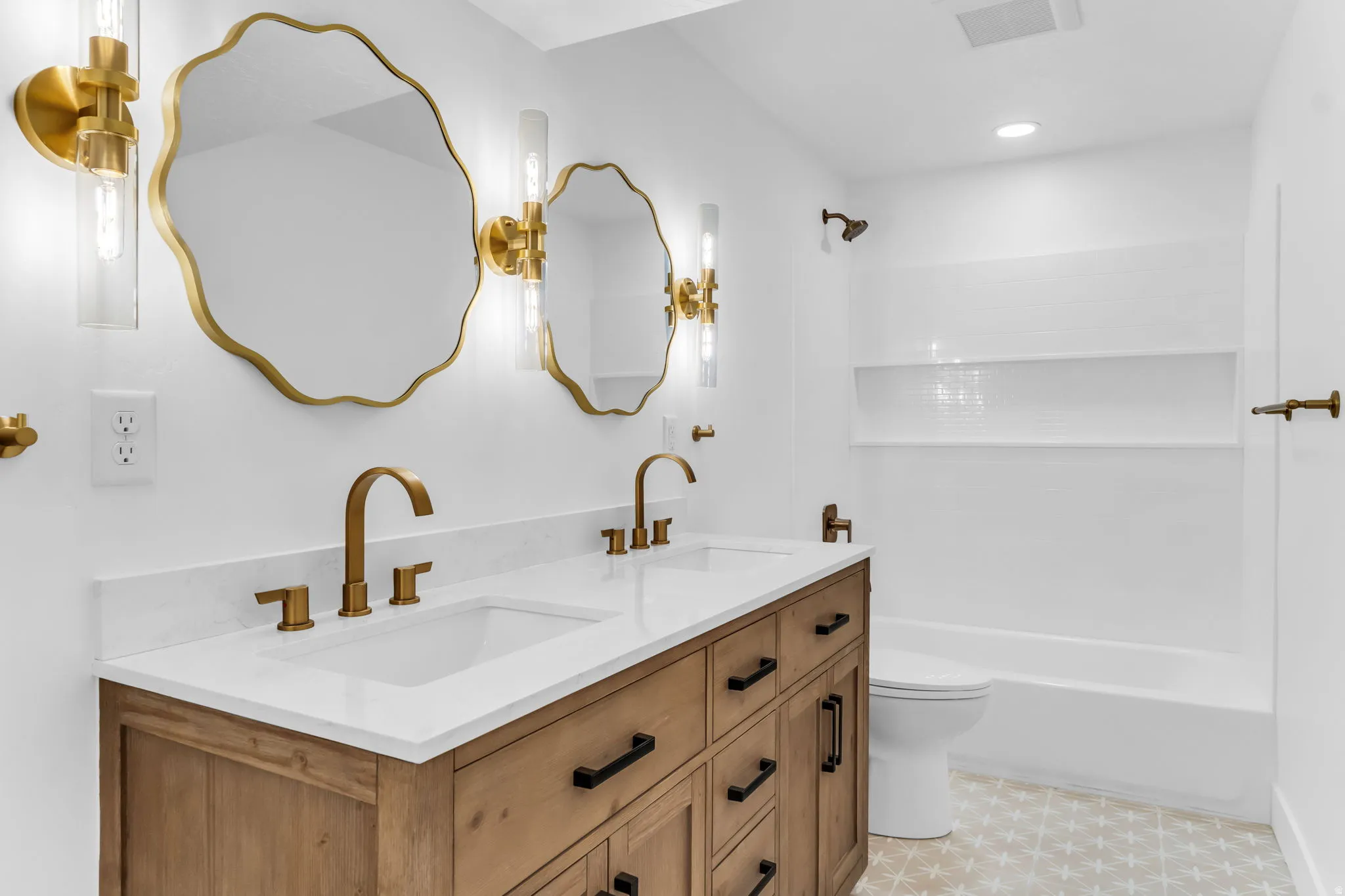 Dual vanity with white countertop, wood-finish cabinetry, and matte brass fixtures