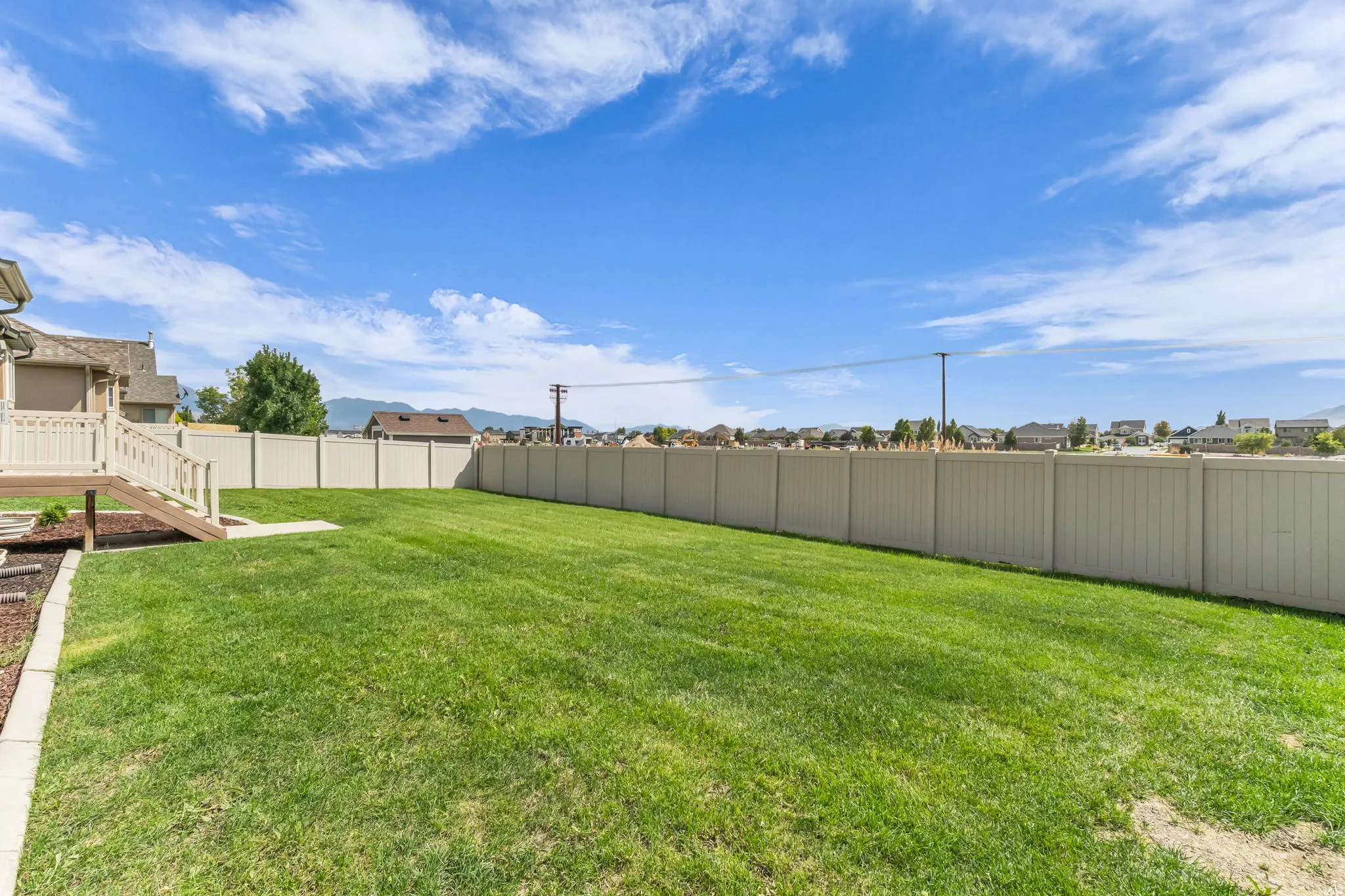 Expansive backyard featuring a lush lawn, privacy fencing, and a multi-level wood deck with stairs