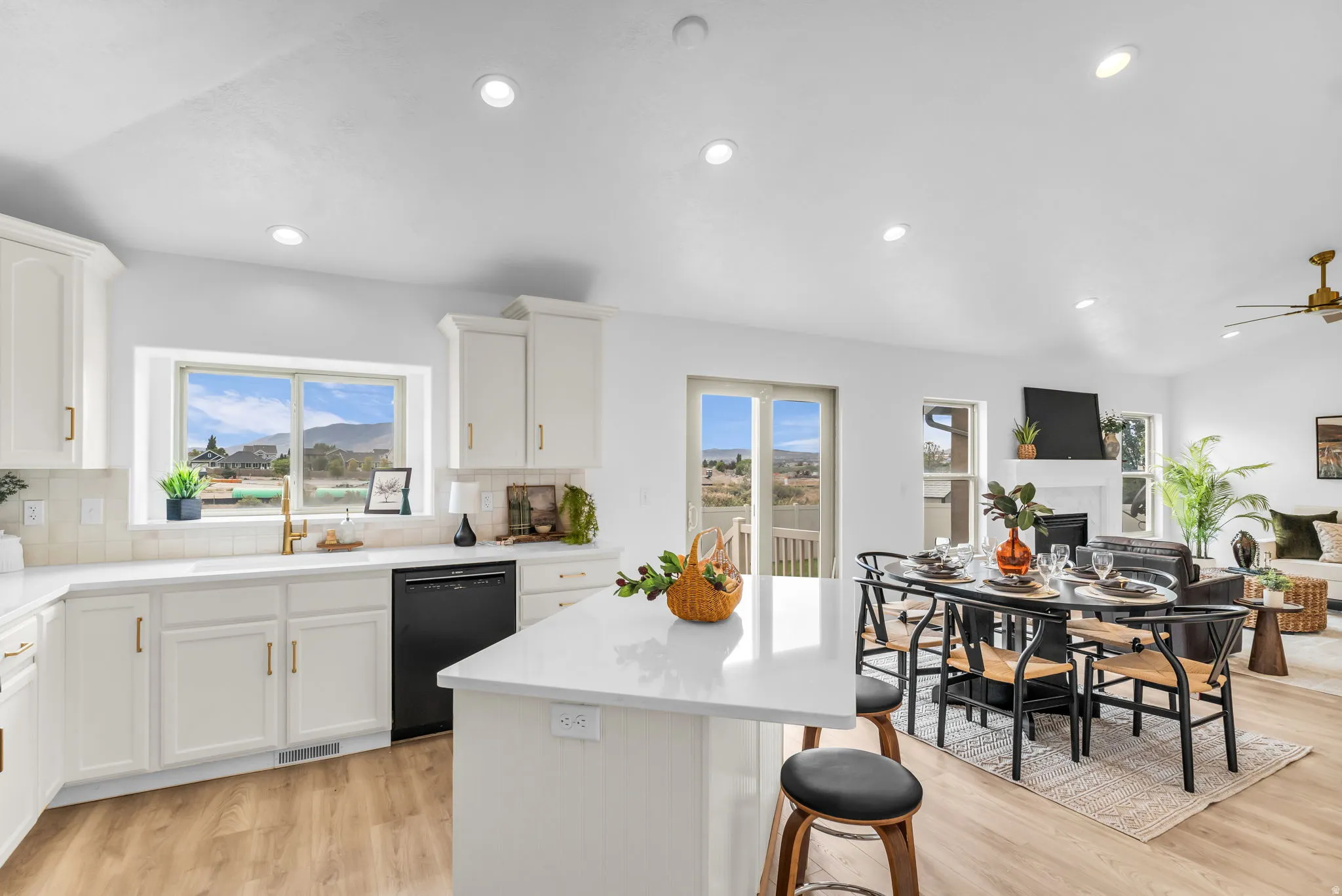 White cabinetry with gold-finish hardware, stainless steel sink with gold-finish fixture, light wood-finish flooring, recessed lighting, and a white stone countertop island