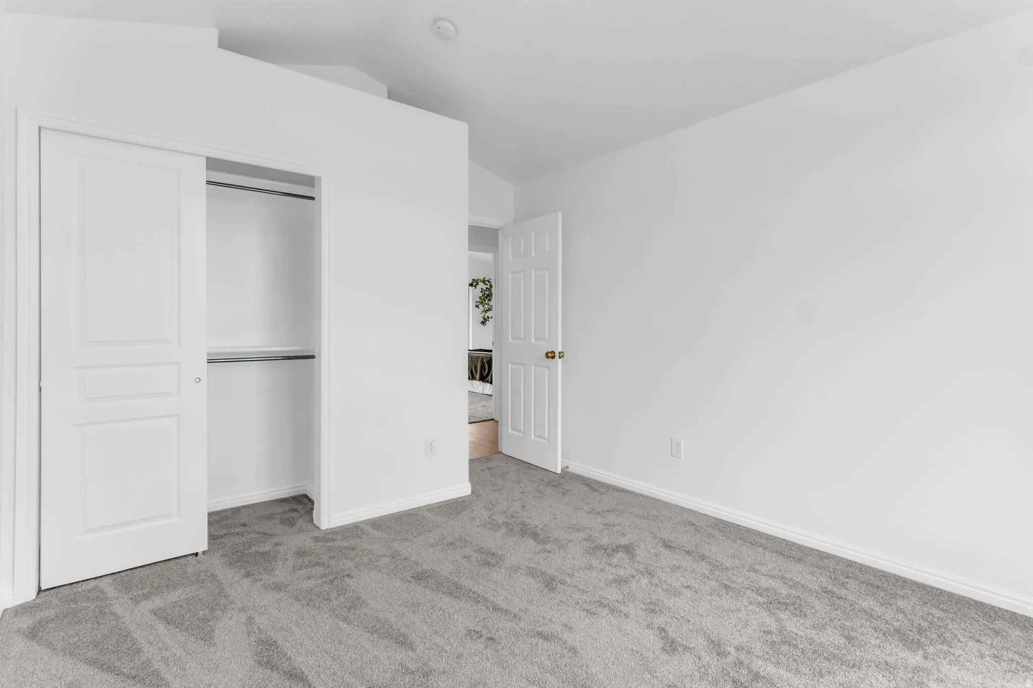 White interior walls, gray carpet flooring, recessed ceiling lighting, a built-in closet with sliding panel doors, and a paneled interior door with brass hardware