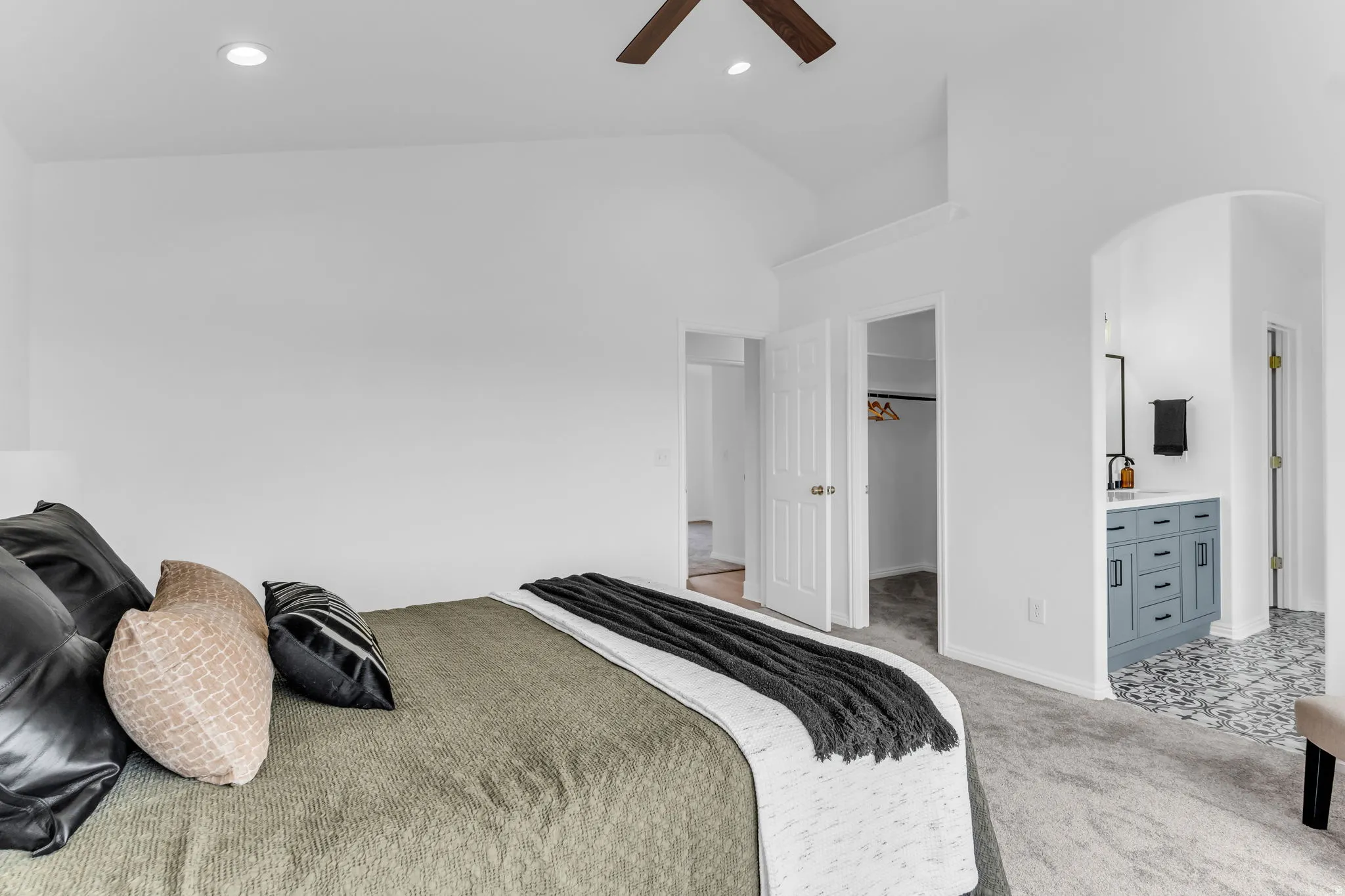 Vaulted ceiling with recessed lighting, ceiling fan, carpet flooring, arched doorway, and a vanity with a rectangular sink