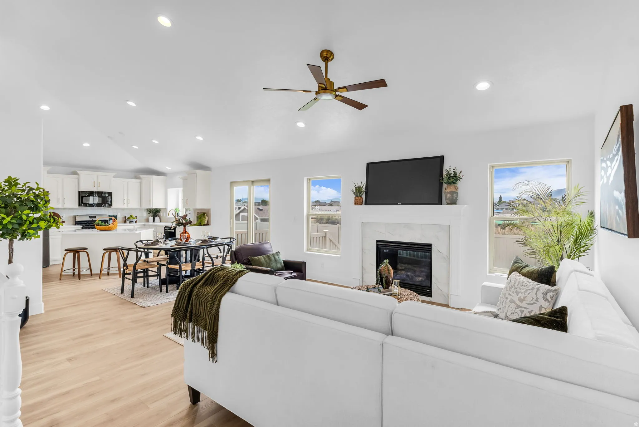 Open-concept living area featuring wood-finish flooring, a fireplace with a stone surround, recessed lighting, and a ceiling fan