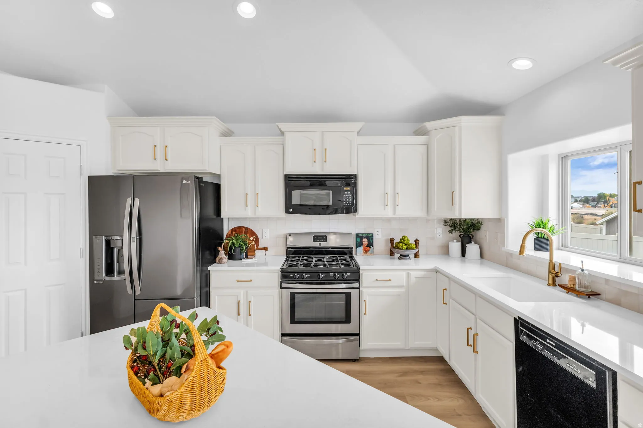 White cabinetry with gold-tone hardware, stainless steel appliances, light-colored countertops, tiled backsplash, and recessed lighting