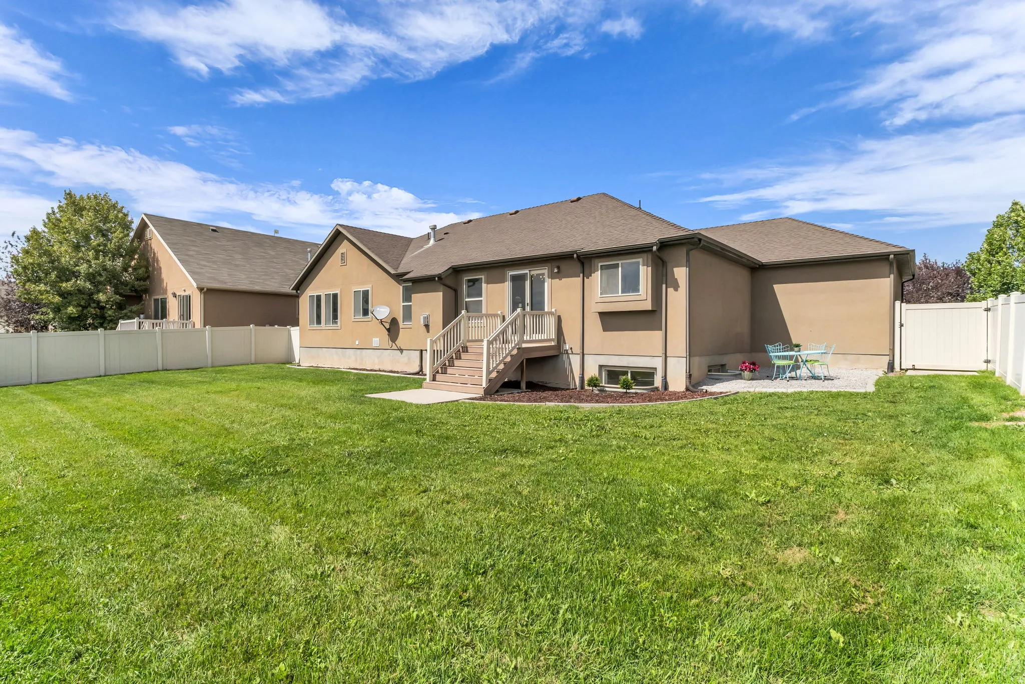 Expansive grassy yard with full vinyl fencing, a ground-level patio, and a raised wood deck