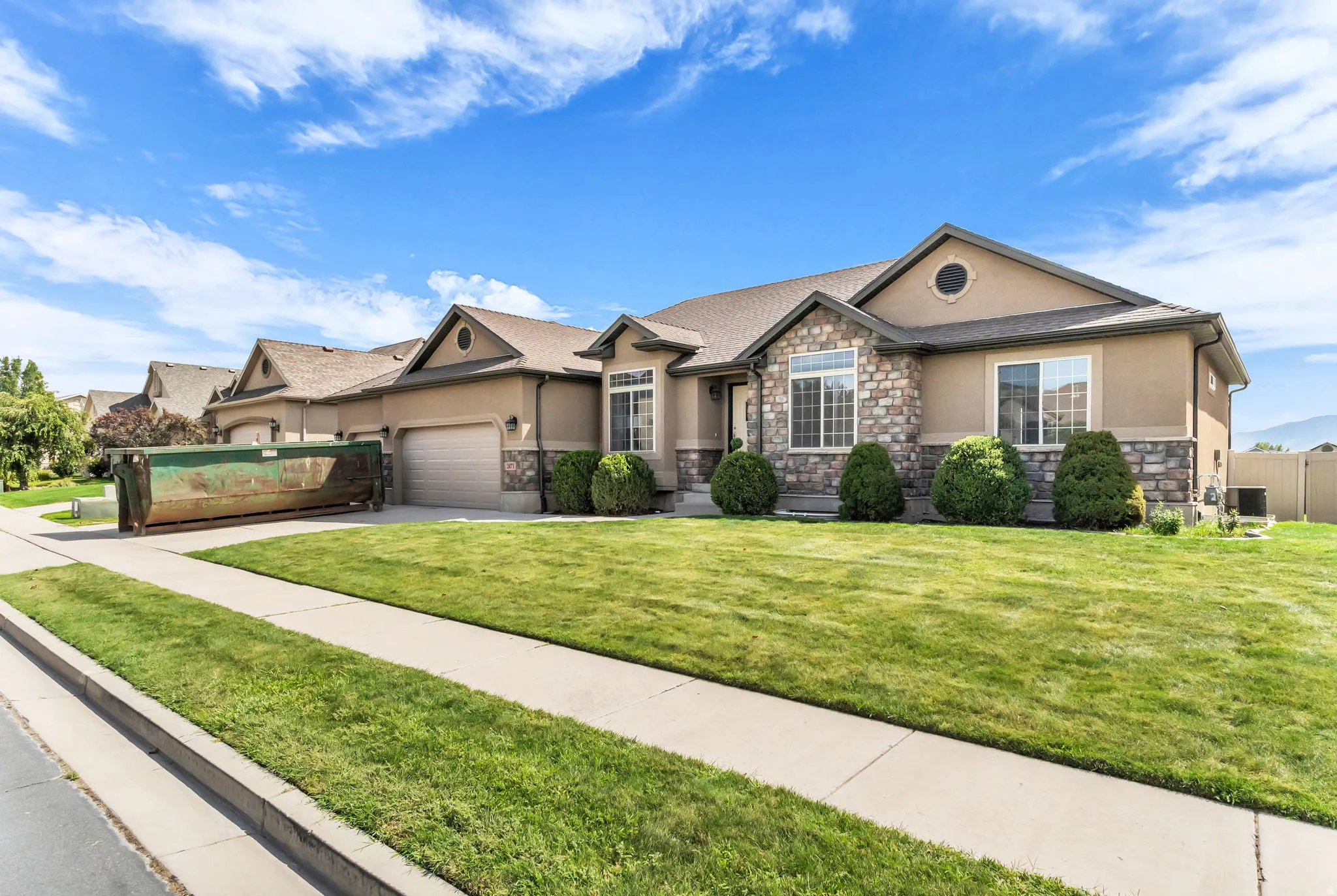 Stucco exterior with stone accents, attached garage, manicured lawn, and mature landscaping