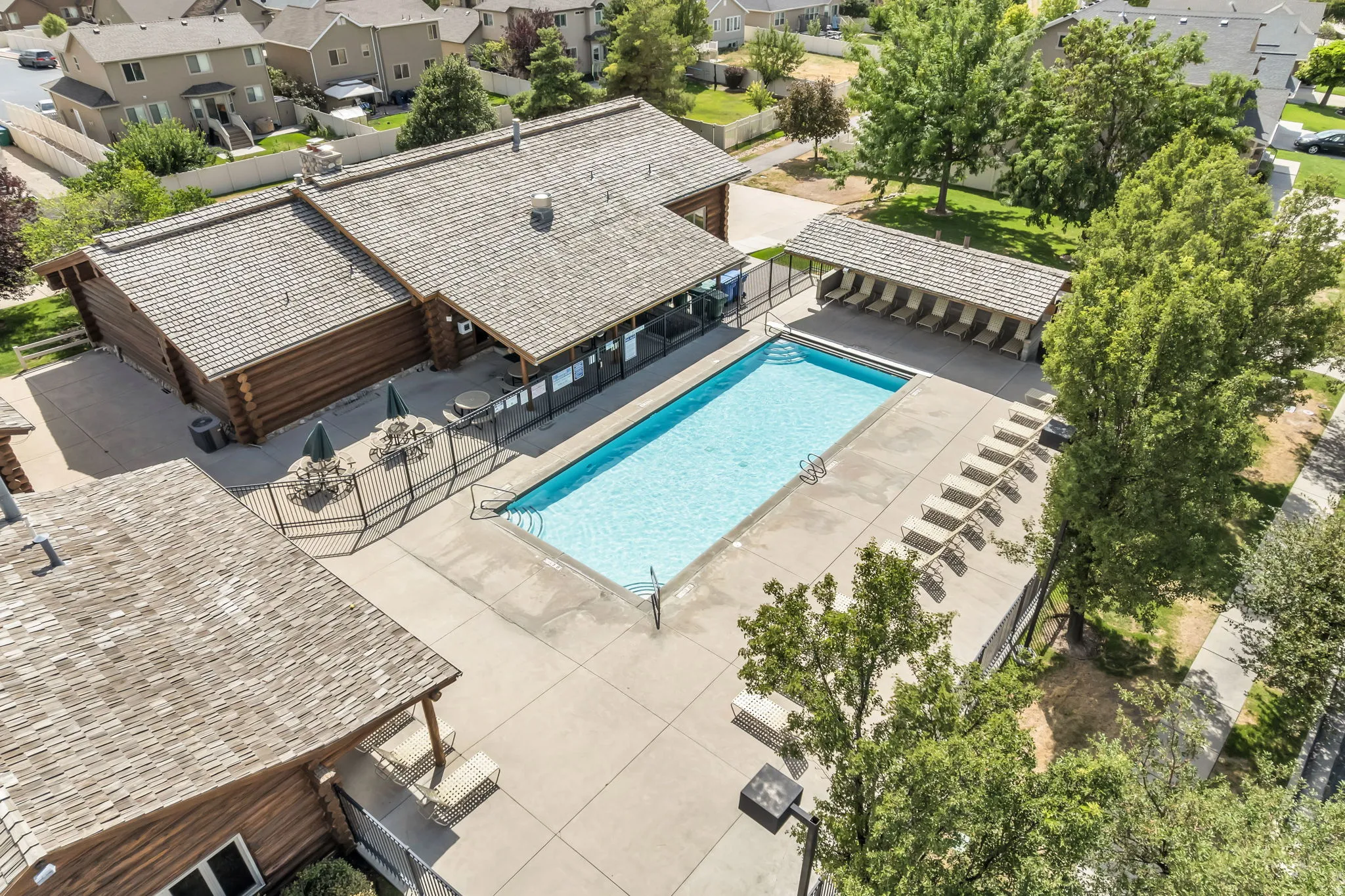 Outdoor swimming pool with a surrounding concrete deck, shaded lounge area, and adjacent log-style clubhouse